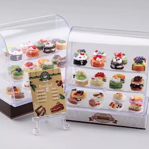 Op de afbeelding: Twee transparante vitrinekasten gevuld met miniatuurtaarten en gebak. De vitrinekast aan de linkerkant heeft een bord met de tekst "Breakfast" en de vitrinekast aan de rechterkant heeft een bord met de tekst "Sweets".