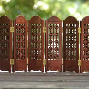 May include: A six-panel wooden room divider with a decorative lattice design. The panels are connected by hinges and are painted a rich mahogany colour.