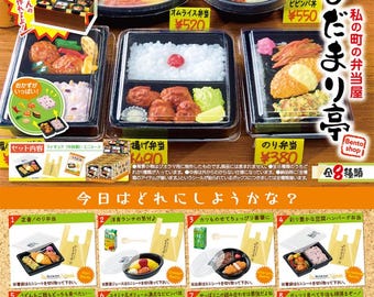 Op de afbeelding: Een kleurrijke illustratie van een Japanse bento-winkel met verschillende lunchboxen, waaronder een gebakken rijst-bento, een omelet-bento, een bibimbap-bento en een zeewier-rijst-bento. De tekst op de afbeelding luidt "De bento-winkel van mijn stad" en "Bento-winkel".