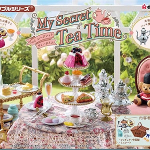 Può includere: Un set da tè in miniatura con un vassoio per torte a tre livelli, un carrello da tè e una teiera d'argento. Il set include una varietà di torte in miniatura, pasticcini e tazze da tè. Il set fa parte della collezione "My Secret Tea Time" di Re-Ment.