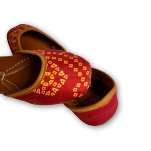 May include: A pair of red fabric shoes with yellow geometric patterns. The shoes have a brown leather trim around the opening.