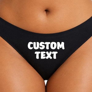 May include: Black underwear with the text "CUSTOM TEXT" in white block letters across the front. The underwear is a low-rise style.