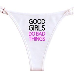 Op de afbeelding: Witte string met dunne bandjes. De tekst "GOOD GIRLS DO BAD THINGS" is gedrukt in zwarte en roze letters. Het ondergoed heeft een eenvoudig, minimalistisch ontwerp.