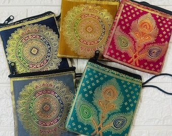 May include: A collection of small, square fabric pouches with intricate gold and colorful embroidered designs. Each pouch has a black zipper and a matching wrist strap. The pouches feature mandala and peacock feather patterns.