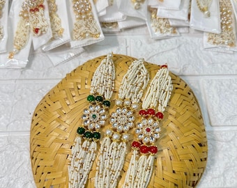 May include: Three white beaded bracelets with gold accents and jeweled flower charms. The charms are green, white, and red.