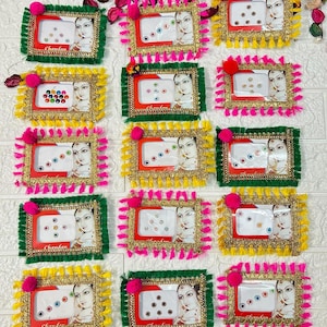 May include: Twelve small, colourful, decorative boxes with gold trim and tassels. Each box contains a set of small, clear, round, adhesive gems. The boxes are arranged in four rows of three boxes each. The boxes are labelled "Chandan".