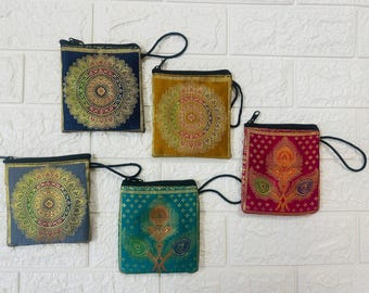 May include: Five small, square fabric pouches in various colors: navy, gold, teal, mustard, and magenta. Each pouch features a decorative gold and red pattern, a black zipper, and a black wrist strap. The pouches are arranged on a white brick background.