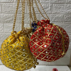 Peut inclure: Plusieurs sacs ronds à cordon de serrage, ornés, de couleurs jaune, rouge et bleu. Les sacs présentent un motif en losange avec de petits miroirs et des bordures dorées. Chaque sac a une poignée perlée.