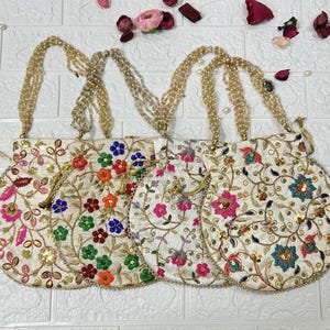 Può includere: Quattro borse a cordoncino in tessuto bianco con ricami colorati e tracolle con perline. Le borse sono decorate con motivi floreali e paillettes.