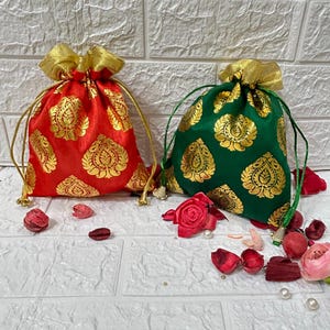 Può includere: Due piccole borse a cordoncino con bordi dorati e un motivo dorato. Una borsa è rossa con accenti dorati e l'altra è verde con accenti dorati.