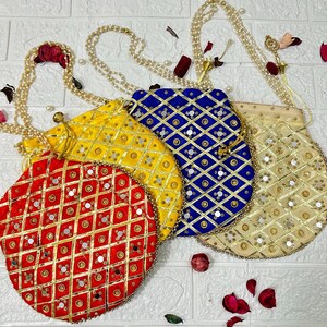 May include: Four colorful, round, beaded bags with pearl-like straps. The bags are red, yellow, blue, and beige, each with a unique geometric pattern and small mirror accents. The bags are arranged on a white brick background.