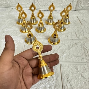 May include: A collection of decorative bells with a gold and silver finish. Each bell features a gold handle with a leaf-like design and a silver-colored bell. The bells are arranged on a white textured surface.