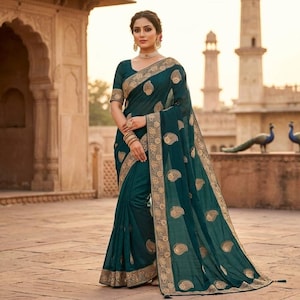 Peut inclure: Un sari de couleur teal avec des motifs cachemire dorés et une bordure dorée. La personne porte le sari devant un bâtiment orné. Le sari a des manches courtes et est drapé avec élégance.