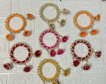 May include: Six colorful bangles with gold accents and dangling charms. The bangles are made of fabric and have a beaded design. The charms are made of fabric and have a flower shape.