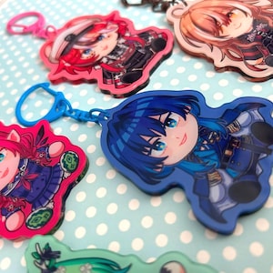 May include: A collection of colorful anime-style character keychains. Each keychain features a unique character design with vibrant colors and detailed artwork. The keychains are attached to metal clasps and rings, ready to be added to keys or bags.