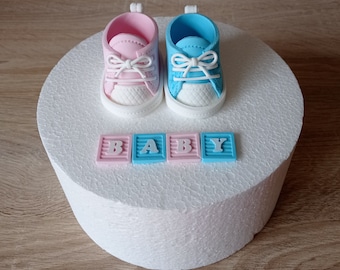 Może przedstawiać: Biały tort ozdobiony niebieskimi i różowymi bucikami dla niemowląt i napisem "BABY" napisanym na klockach.
