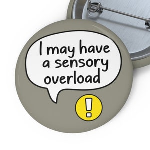 May include: A grey button with a white speech bubble that says "I may have a sensory overload" and a yellow exclamation mark inside a circle.
