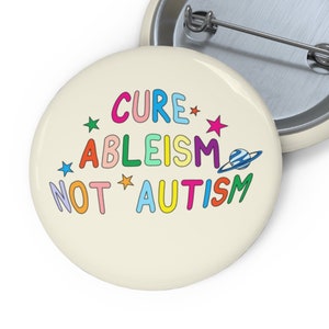 May include: A white button with the text "Cure ableism not autism" in rainbow colours with stars and a planet graphic.