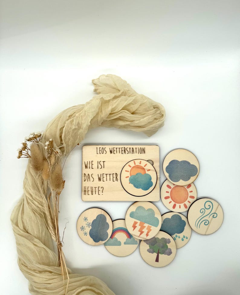 May include: Wooden weather station toy with the text "LEOS WETTERSTATION" and "WIE IST DAS WETTER HEUTE?" includes weather symbols like sun, clouds, rain, and snow. The set has a light wood finish and colorful illustrations.