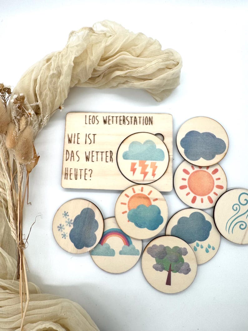 May include: Wooden weather station toy with the text "LEOS WETTERSTATION WIE IST DAS WETTER HEUTE?" includes a wooden board with a cutout for weather symbols. Round wooden tokens depict weather elements like sun, clouds, rain, and rainbow.
