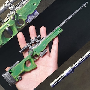 Op de afbeelding: Een groene en zwarte speelgoed-scharfschuttersgeweer met een richtkijker. Het geweer wordt in de hand van een persoon gehouden.