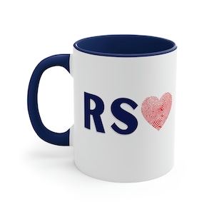 Puede incluir: Taza de cerámica blanca con borde y asa azul marino. La taza tiene las letras "RS" en azul marino y un corazón rojo en forma de huella dactilar.