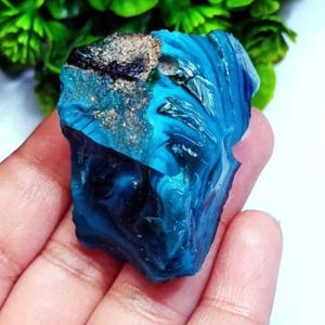Puede incluir: Una piedra preciosa azul y negra con patrones en espiral. La piedra preciosa es rugosa y tiene un aspecto natural sin pulir.