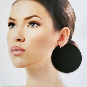 Puede incluir: Un par de pendientes grandes, redondos y negros. Los pendientes están hechos de un material liso y sólido.