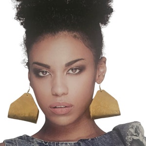 以下が含まれることがあります： アフロヘアの女性が、花柄の大きなゴールドのイヤリングをしています。イヤリングは三角形です。