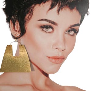 May include: A pair of large, gold-toned, geometric earrings with a hammered texture. The earrings are shaped like a rectangle with a cut-out in the center.