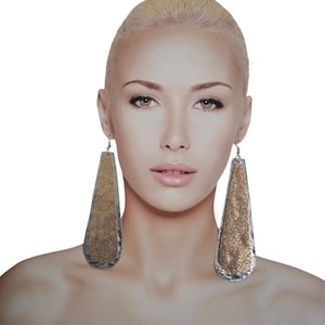 以下が含まれることがあります： 銀色のフレームと金色のテクスチャ加工された表面を持つ、長い涙滴型のイヤリングのペアです。