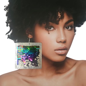 May include: Large, square earrings with a silver frame and colorful sequins. The sequins display a gradient of colors, including blue, green, purple, and pink. The earrings are hanging from a silver hook.