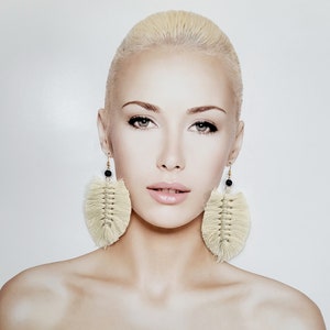 Puede incluir: Pendientes de macramé color crema con forma de hoja y detalles de cuentas negras. Los pendientes cuelgan de ganchos dorados. Un accesorio de estilo bohemio.