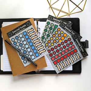 May include: Four sheets of colourful stickers with a grid pattern and various shapes, including dice and banners. The stickers are labelled "Journal Icons" and "by: Crit Happens Dice".