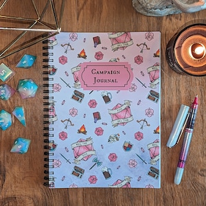 May include: A white spiral bound journal with a pink and blue pattern of dice, swords, and other fantasy game symbols. The cover reads "Campaign Journal".
