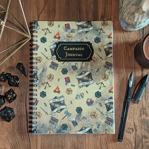 May include: A spiral bound notebook with a yellow and brown cover featuring a repeating pattern of dice, swords, shields, and other fantasy-themed illustrations. The cover has the text "Campaign Journal" in black lettering.