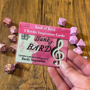 May include: A pink and green card with the text "Bank of Bard" and "5 Bardic Inspiration Cards". The card also features a treble clef and the text "Bank of BARD".
