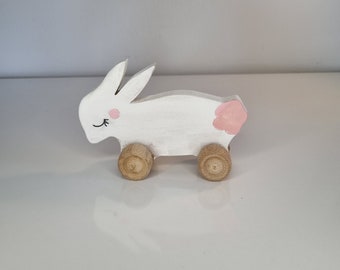 May include: White wooden bunny pull toy with pink painted details and brown wooden wheels.