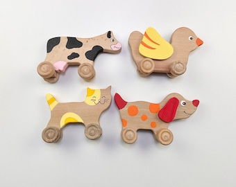 May include: Four wooden toy animals on wheels. A brown cow with black spots, a brown cat with yellow spots, a brown dog with orange spots, and a brown bird with yellow wings.