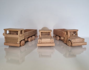 May include: Three wooden toy trucks, one with a flatbed, one with a cement mixer, and one with a dump bed. The trucks are all made of natural wood and have a rustic look.