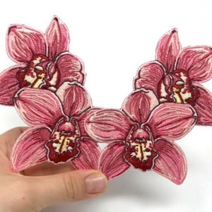 Peut inclure: Patch brodé de fleurs d'orchidées roses. Le patch est en tissu et présente un design détaillé. Il est parfait pour ajouter une touche d'élégance à tout projet.