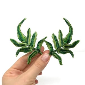 May include: Two green embroidered leaf patches, ideal for adding a touch of nature to clothing or crafts.