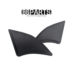 Op de afbeelding: Twee zwarte, driehoekige auto-onderdelen worden getoond tegen een witte achtergrond. De onderdelen zijn gevormd als kleine vleugels of vinnen. De tekst "86PARTS" en "the ART of engineering" zijn in zwart boven de onderdelen gedrukt.