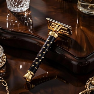 May include: A gold and black safety razor with a patterned handle. The razor features a gold head and accents, with a black handle adorned with gold-colored oval inlays. The razor is displayed on a dark, polished surface.