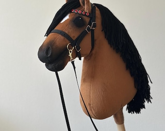 May include: A brown plush hobby horse with a black mane and tail. The horse has a black bridle with red accents and a black rein. The horse is mounted on a wooden stick.