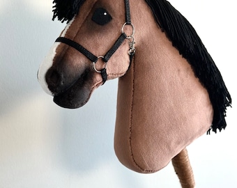 Puede incluir: Una cabeza de caballo de peluche marrón y blanco con una crin negra y un bozal negro. La cabeza del caballo está unida a un palo de madera.