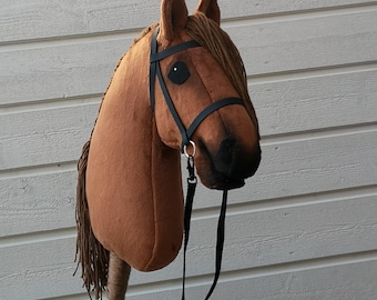 May include: A brown plush horse head with a black bridle and reins. The horse head is attached to a wooden stick.