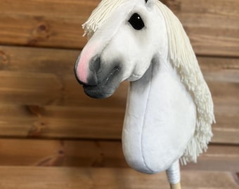 May include: White plush horse head on a wooden stick. The horse has black eyes and a pink nose.
