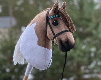 May include: A brown and white horse head with a black bridle and blue gem accents. The horse head is attached to a wooden stick and a black rein.
