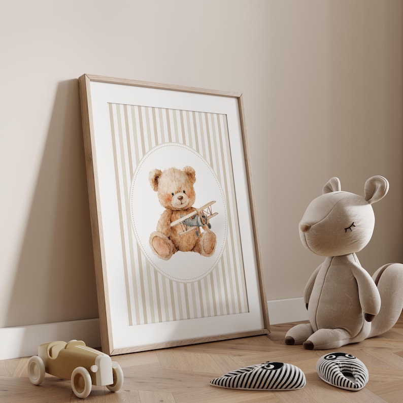 May include: A framed print featuring a watercolor illustration of a teddy bear holding a toy airplane. The artwork is set against a striped background in a neutral color palette. A wooden toy car and a stuffed squirrel are in the foreground.